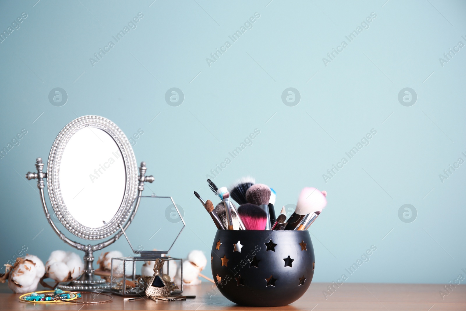 Photo of Holder with professional makeup brushes and mirror on table near color wall