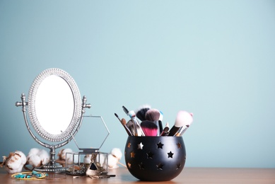 Photo of Holder with professional makeup brushes and mirror on table near color wall