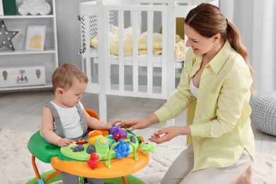 Mother and her little son spending time together at home. Cute baby making first steps with toy walker