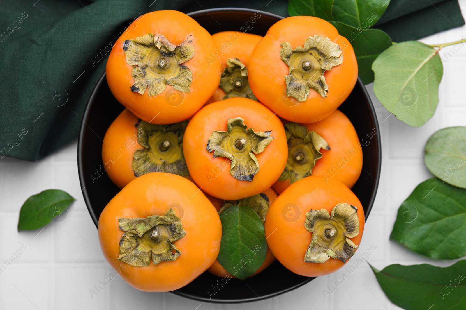 Photo of Bowl with delicious ripe juicy persimmons on white table, flat lay