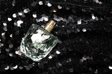 Photo of Luxury perfume in bottle on fabric with shiny sequins, top view