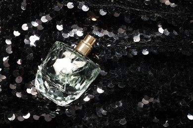 Luxury perfume in bottle on fabric with shiny sequins, top view