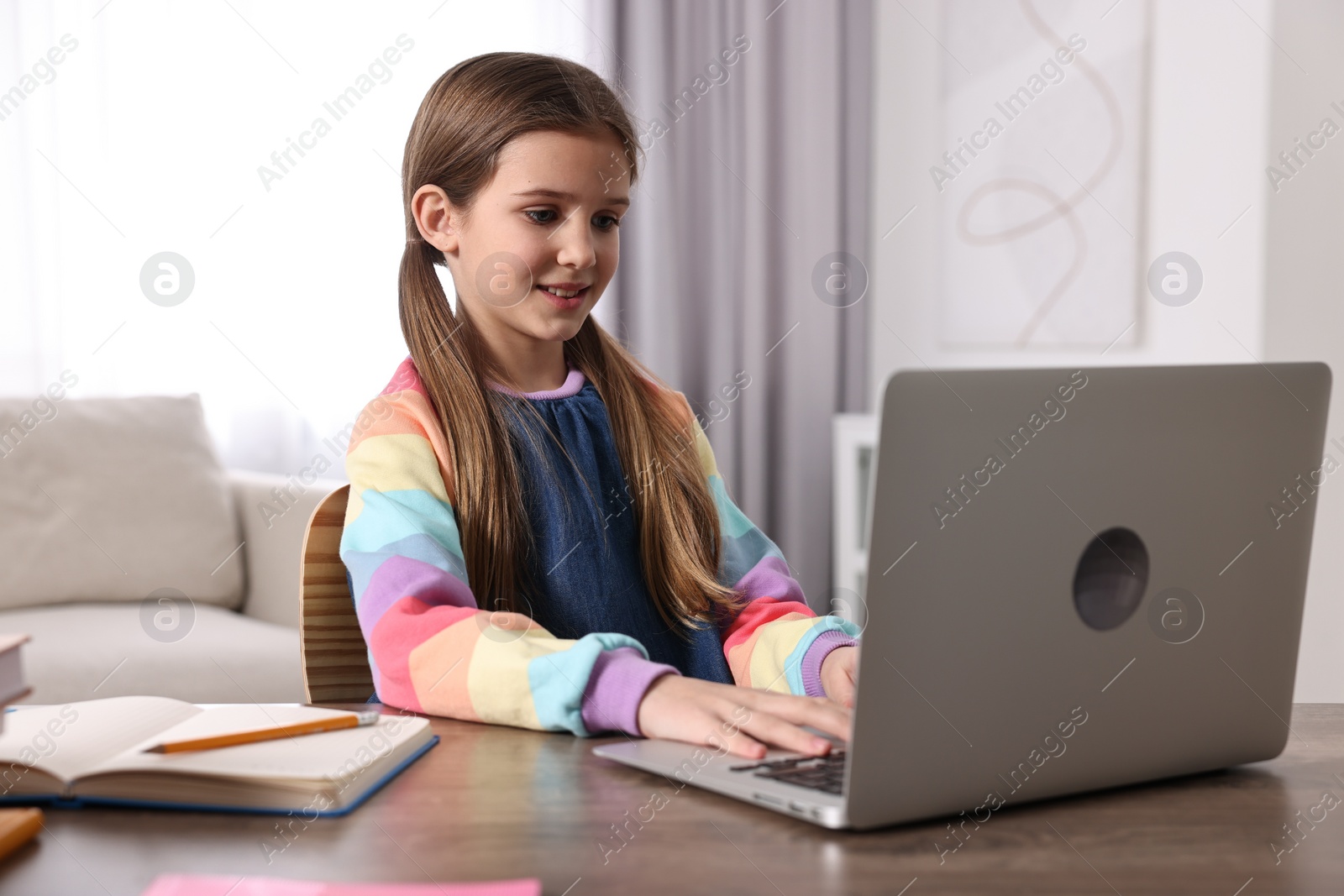 Photo of E-learning. Cute girl using laptop during online lesson at table indoors