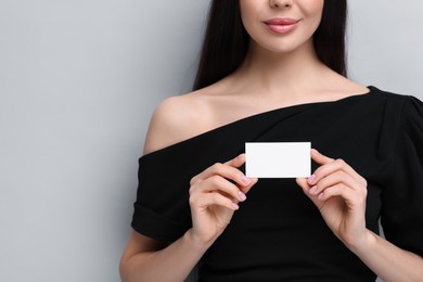 Photo of Woman holding blank business card on light grey background, closeup. Space for text
