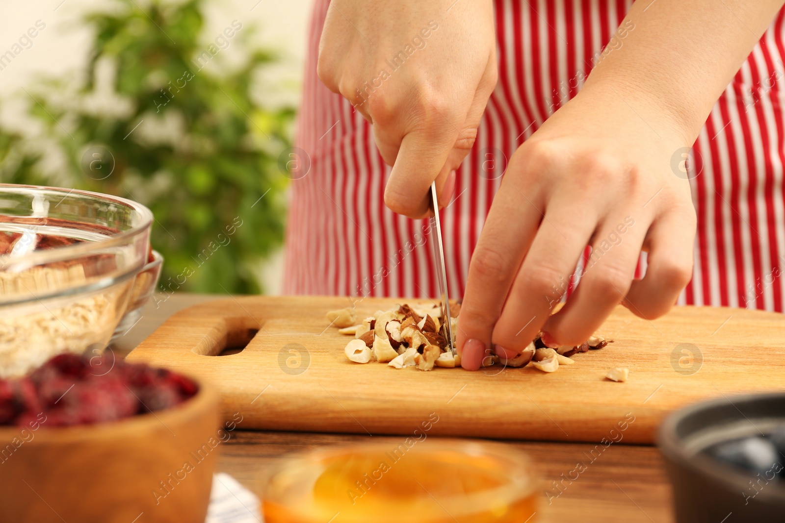 Photo of Making granola. Woman cutting nuts at table in kitchen, closeup