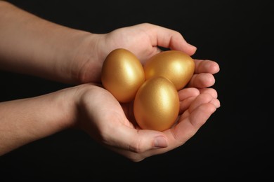 Photo of Woman holding shiny golden eggs on black background, closeup