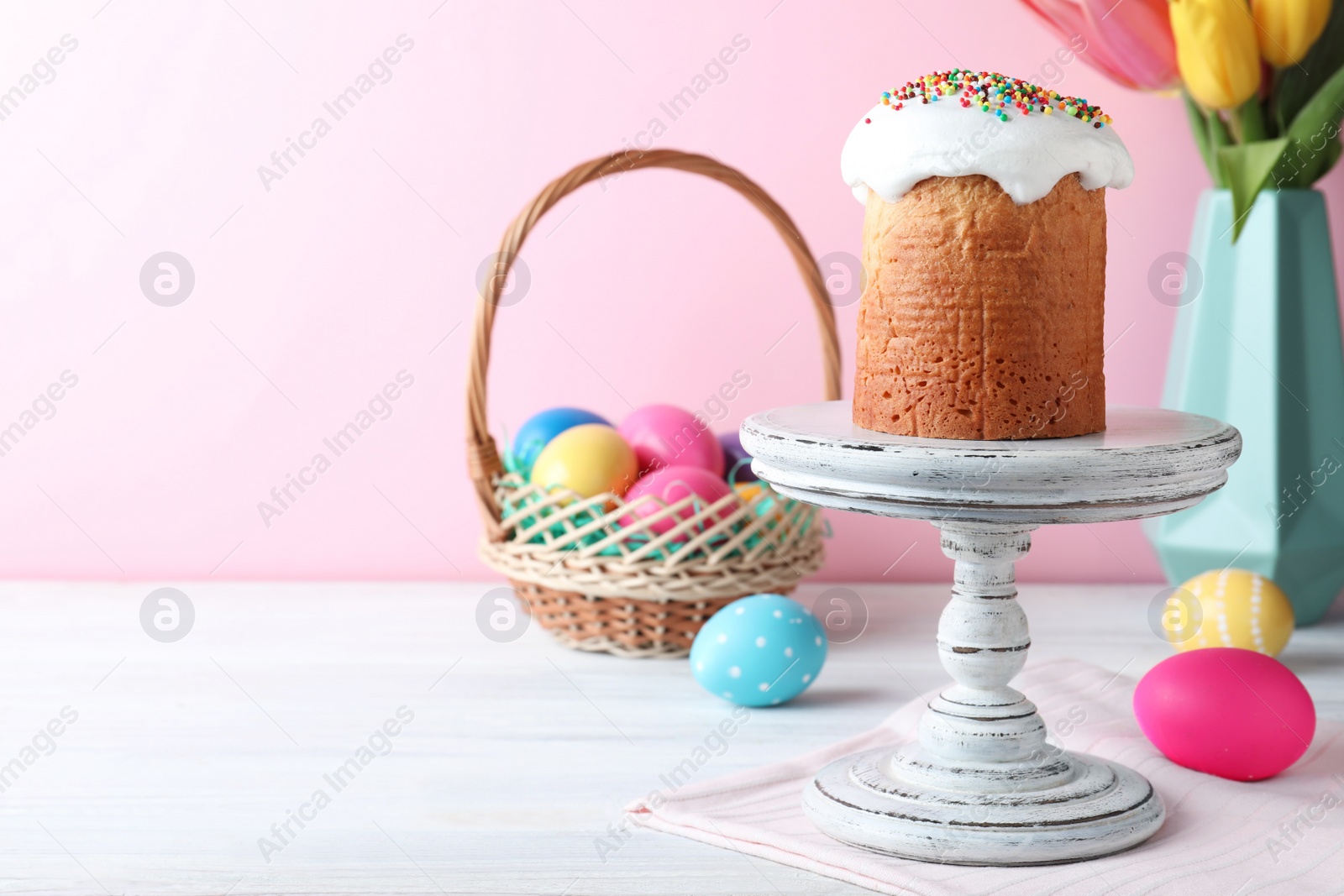 Photo of Easter cake, colorful eggs and tulips on white wooden table, space for text