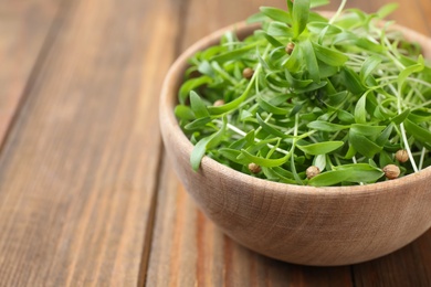 Photo of Bowl with fresh microgreen on wooden table, closeup. Space for text