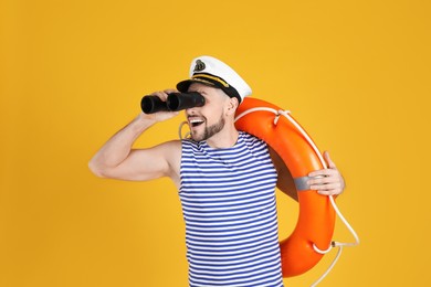 Photo of Sailor with orange ring buoy looking through binoculars on yellow background