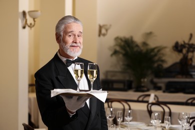 Photo of Senior butler holding tray with glasses of sparkling wine in restaurant. Space for text