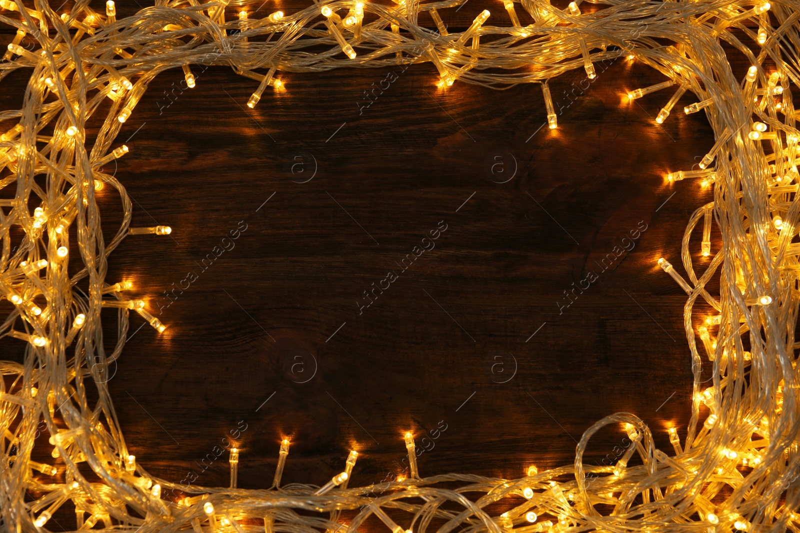 Photo of Frame made of glowing Christmas lights on wooden background, top view. Space for text