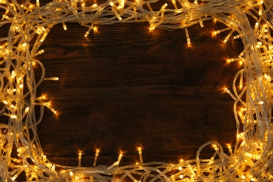 Photo of Frame made of glowing Christmas lights on wooden background, top view. Space for text