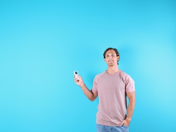 Young man with air conditioner remote on color background, copy space text