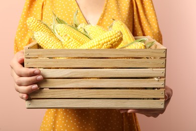 Photo of Woman with crate of corn cobs on coral background, closeup