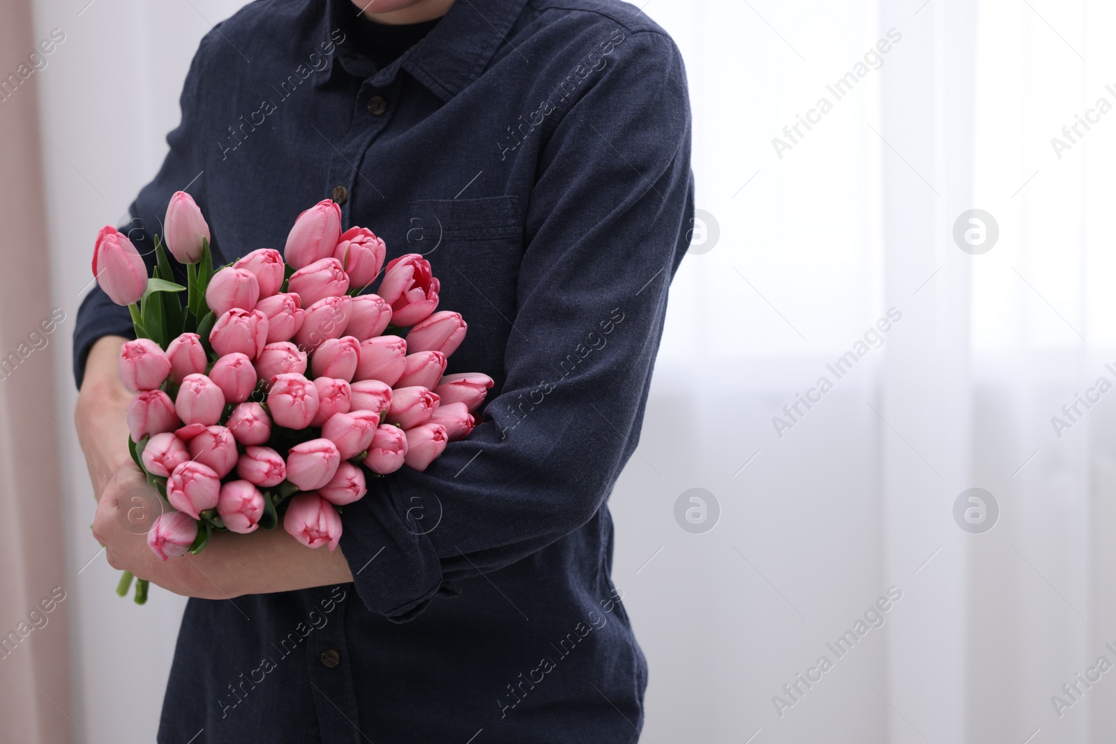 Photo of Woman holding bouquet of pink tulips indoors, closeup. Space for text