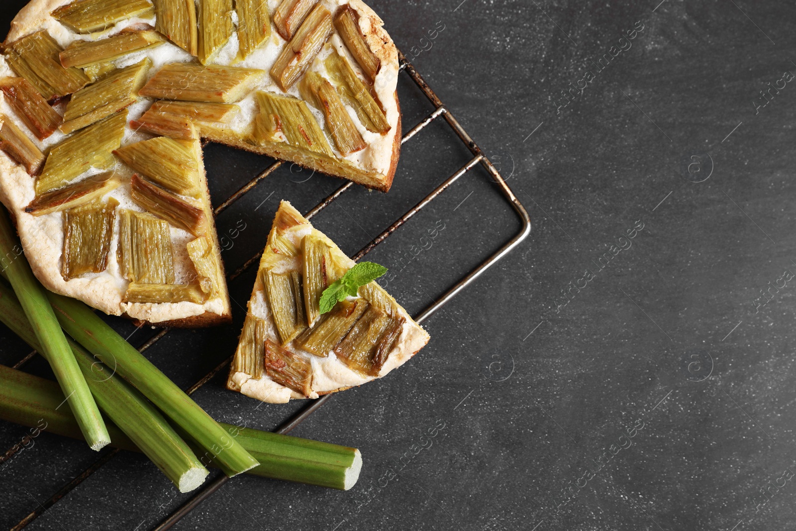 Photo of Freshly baked rhubarb pie and stalks on black table, flat lay. Space for text