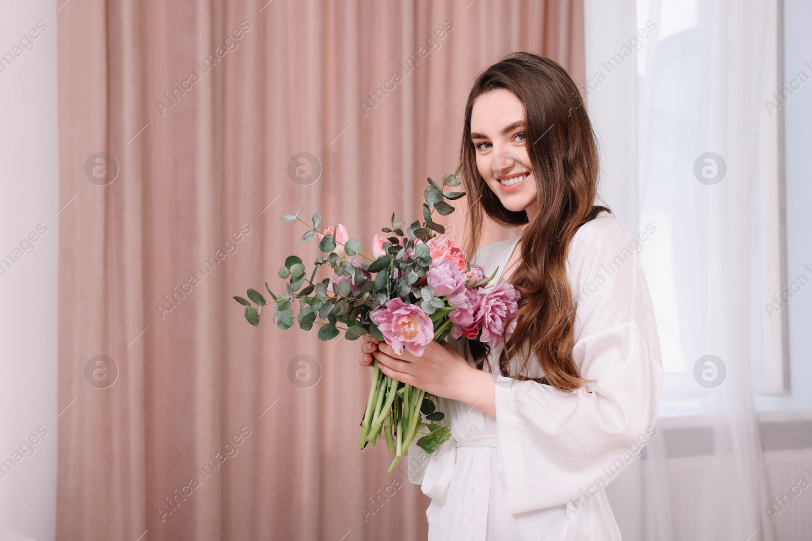 Photo of Beautiful happy young woman with bouquet of flowers indoors