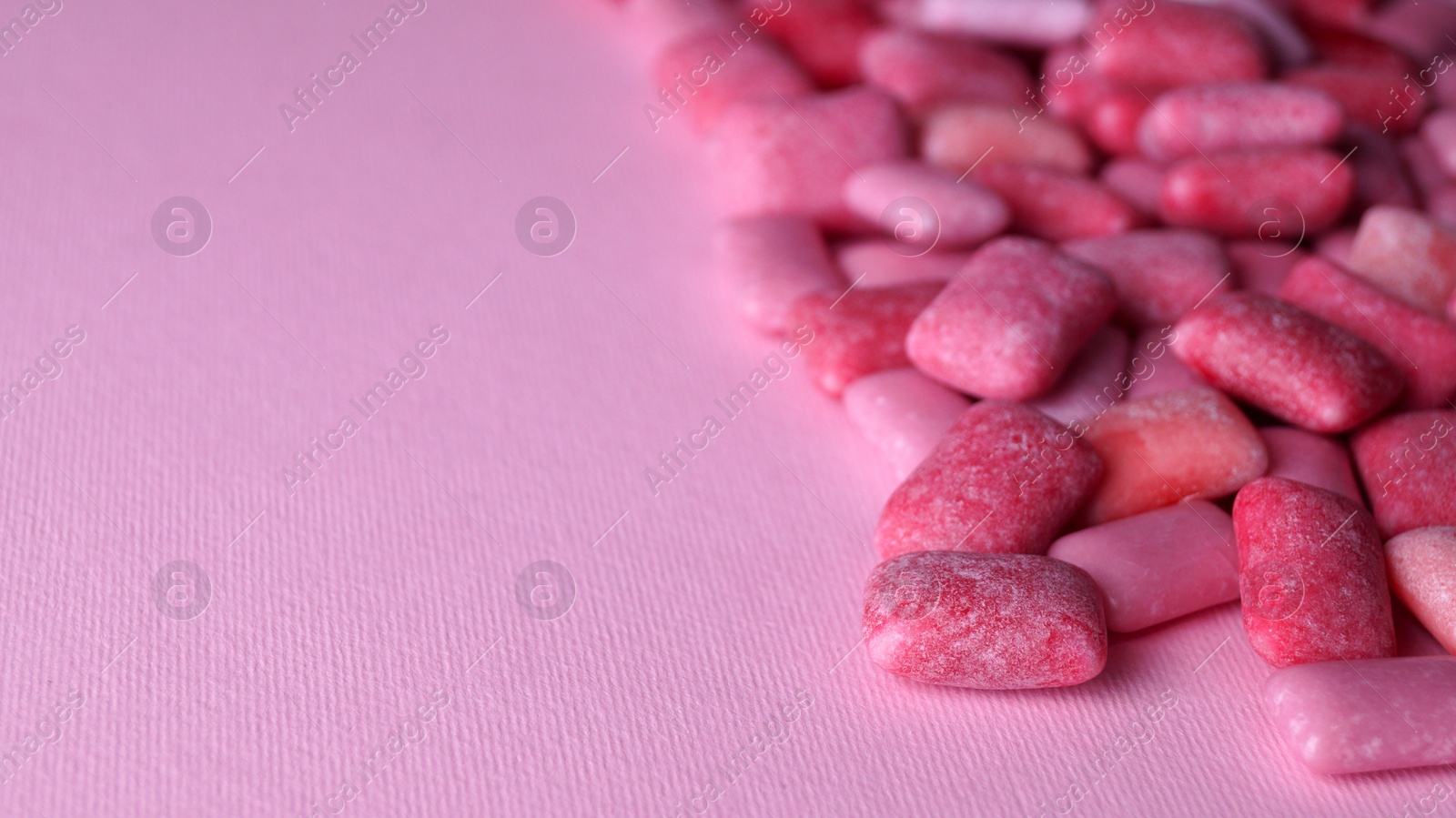 Photo of Heap of tasty sweet chewing gums on pink background, closeup. Space for text