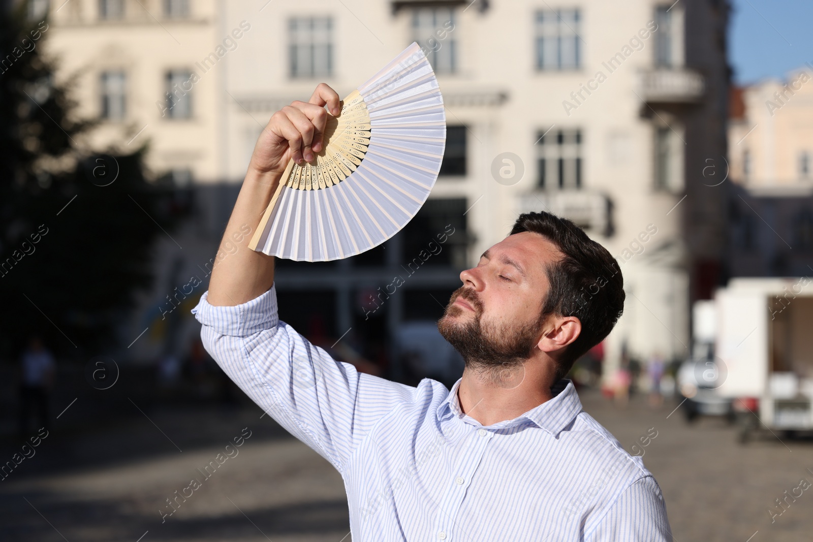 Photo of Man with hand fan suffering from heat outdoors