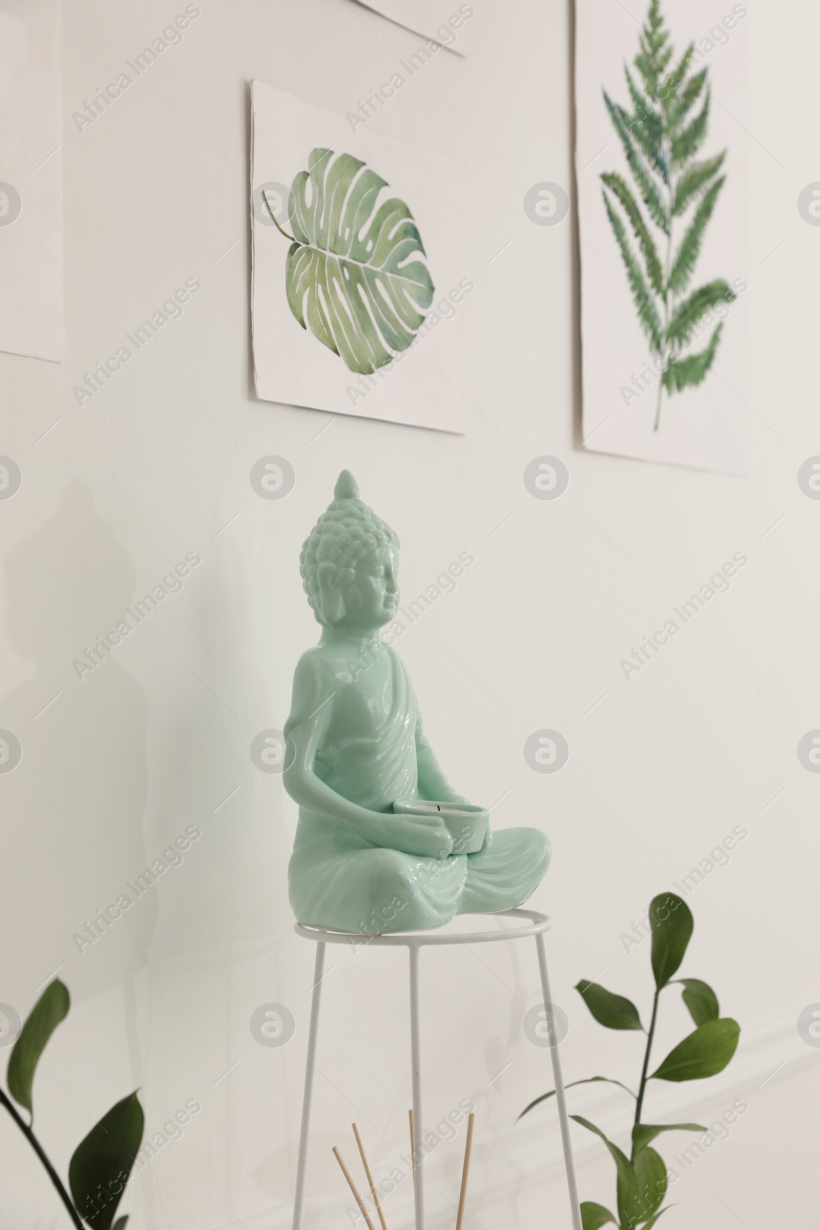 Photo of Ceramic Buddha sculpture near wall with floral paintings indoors. Interior design