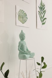 Ceramic Buddha sculpture near wall with floral paintings indoors. Interior design