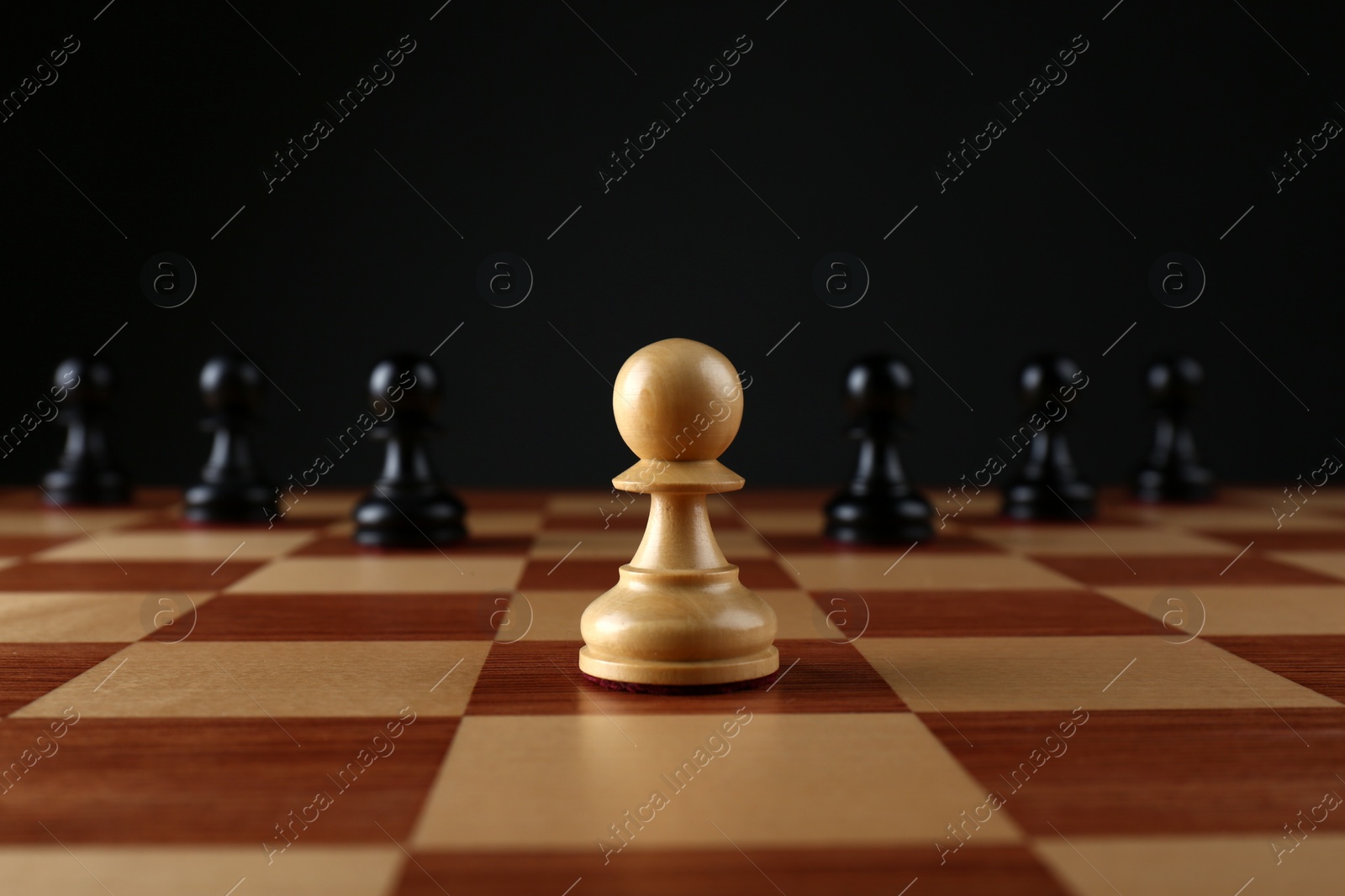 Photo of White pawn in front of black ones on wooden chess board against dark background