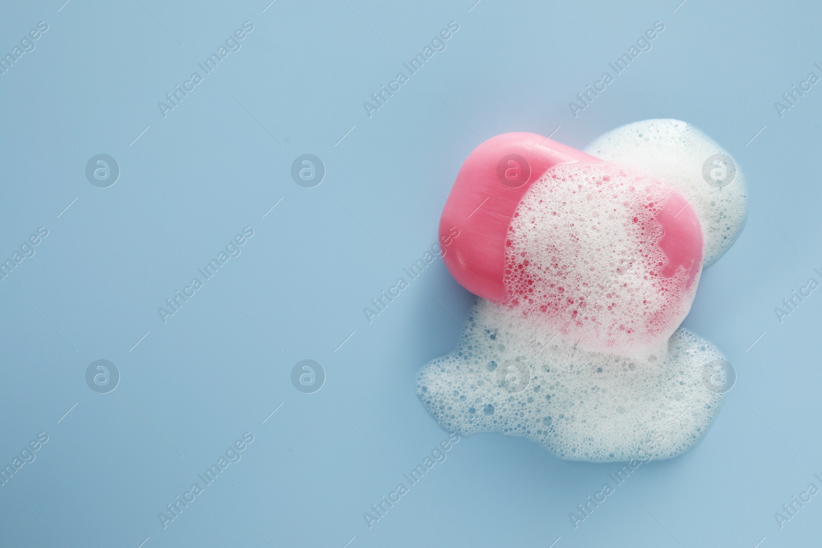 Photo of Soap bar with fluffy foam on light blue background, top view. Space for text