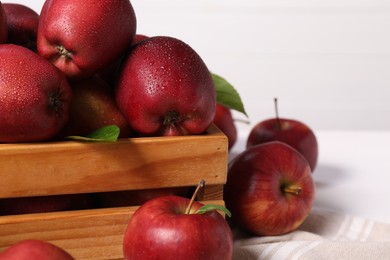 Fresh red apples in wooden crate on white table, closeup. Space for text