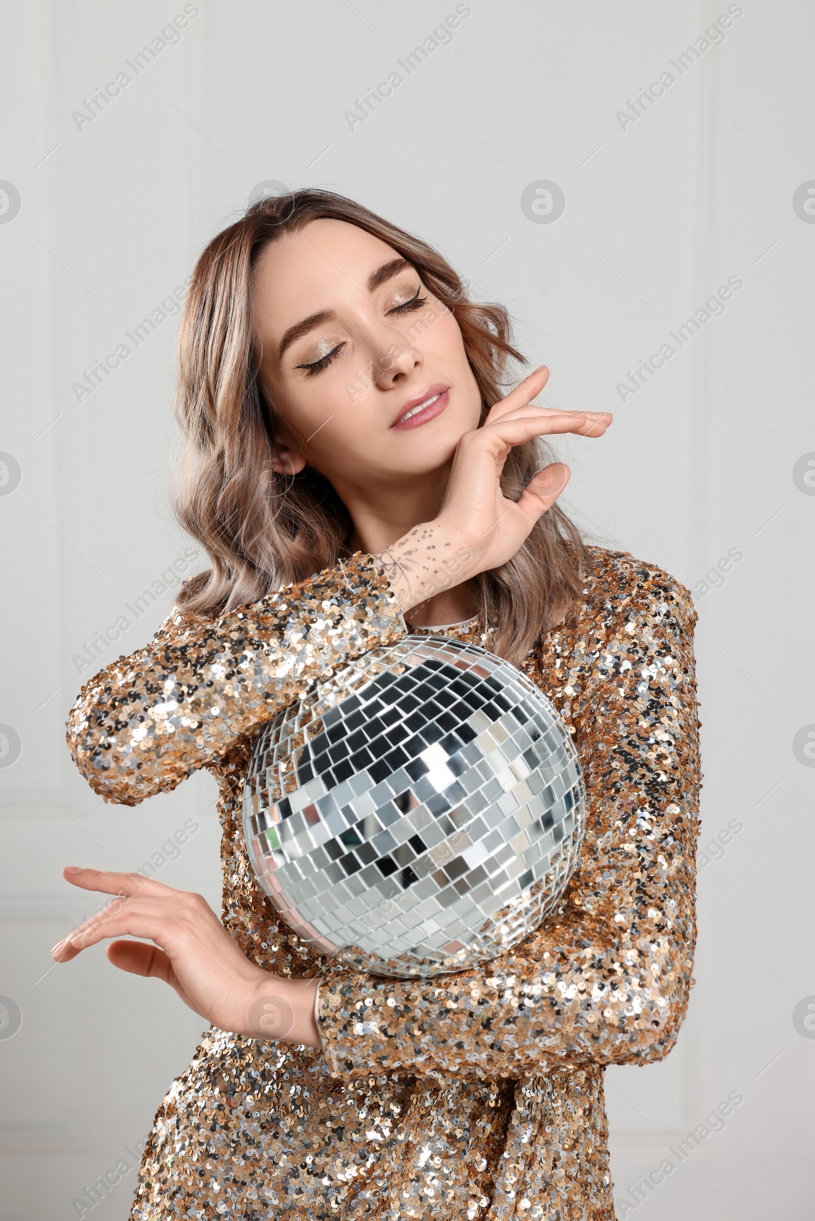 Photo of Beautiful woman in golden dress with disco ball posing on white background