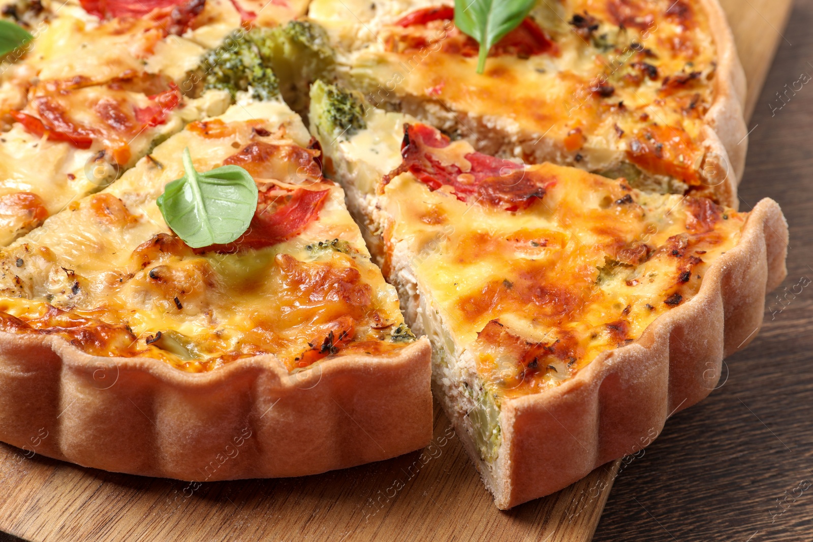 Photo of Tasty quiche with tomatoes, basil and cheese on wooden table, closeup