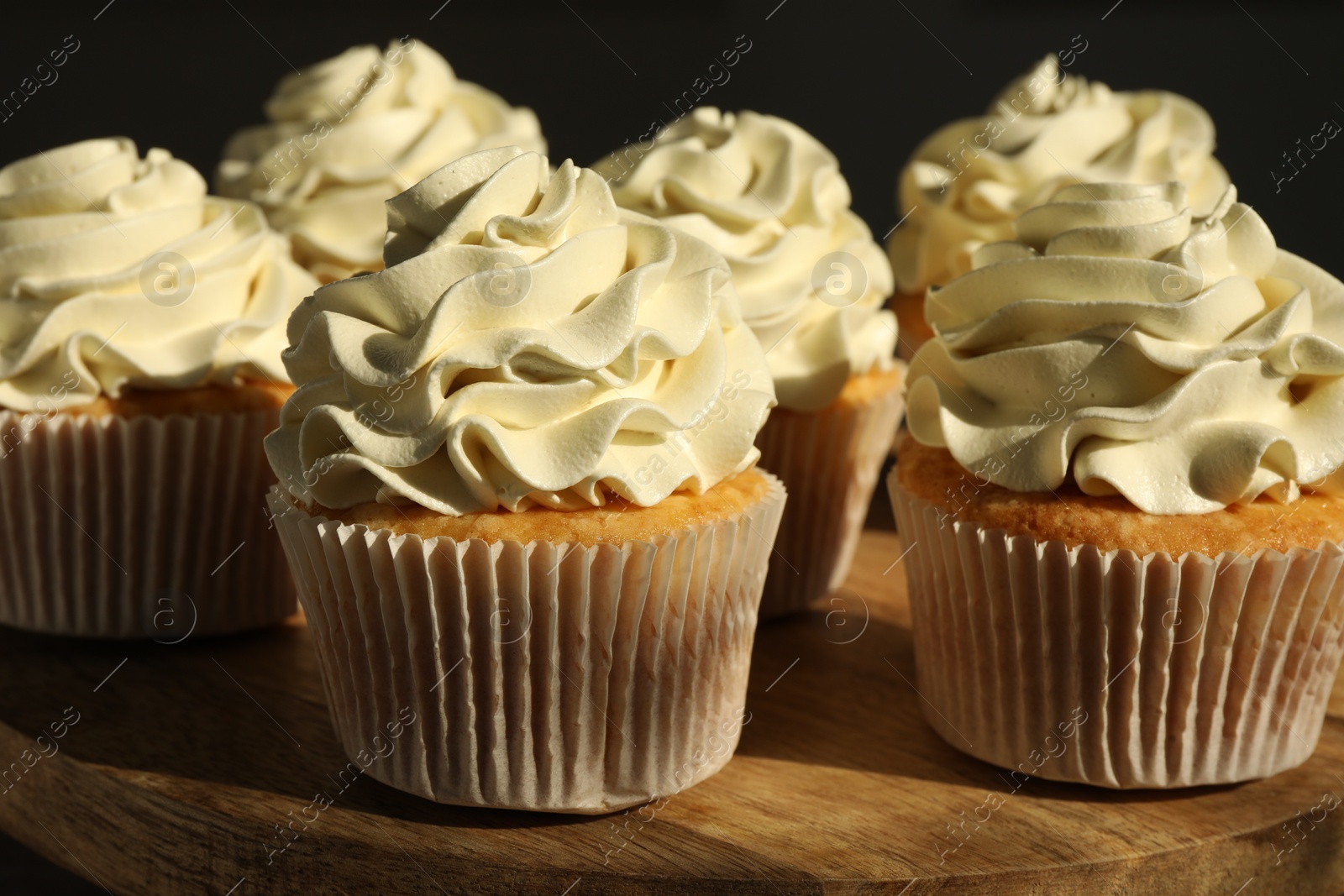 Photo of Tasty cupcakes with vanilla cream on wooden stand, closeup