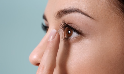 Photo of Young woman putting contact lens in her eye on color background
