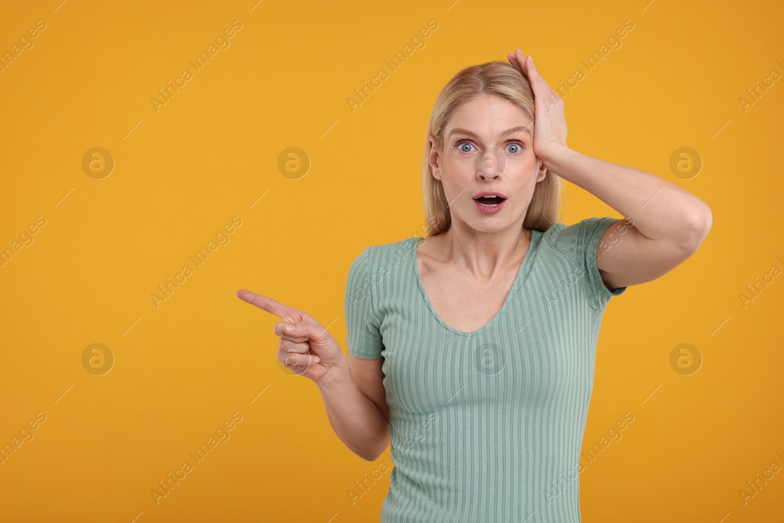 Photo of Surprised woman pointing at something on yellow background, space for text