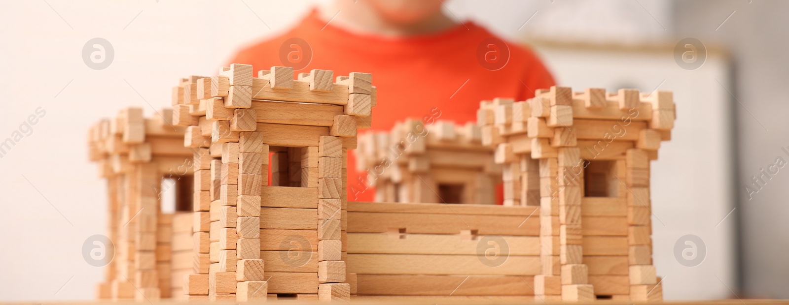 Photo of Little boy playing with wooden fortress indoors, closeup. Child's toy