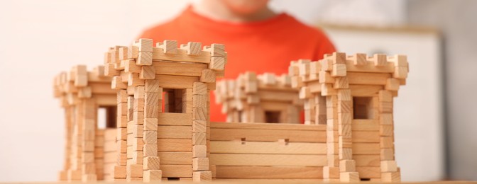 Photo of Little boy playing with wooden fortress indoors, closeup. Child's toy