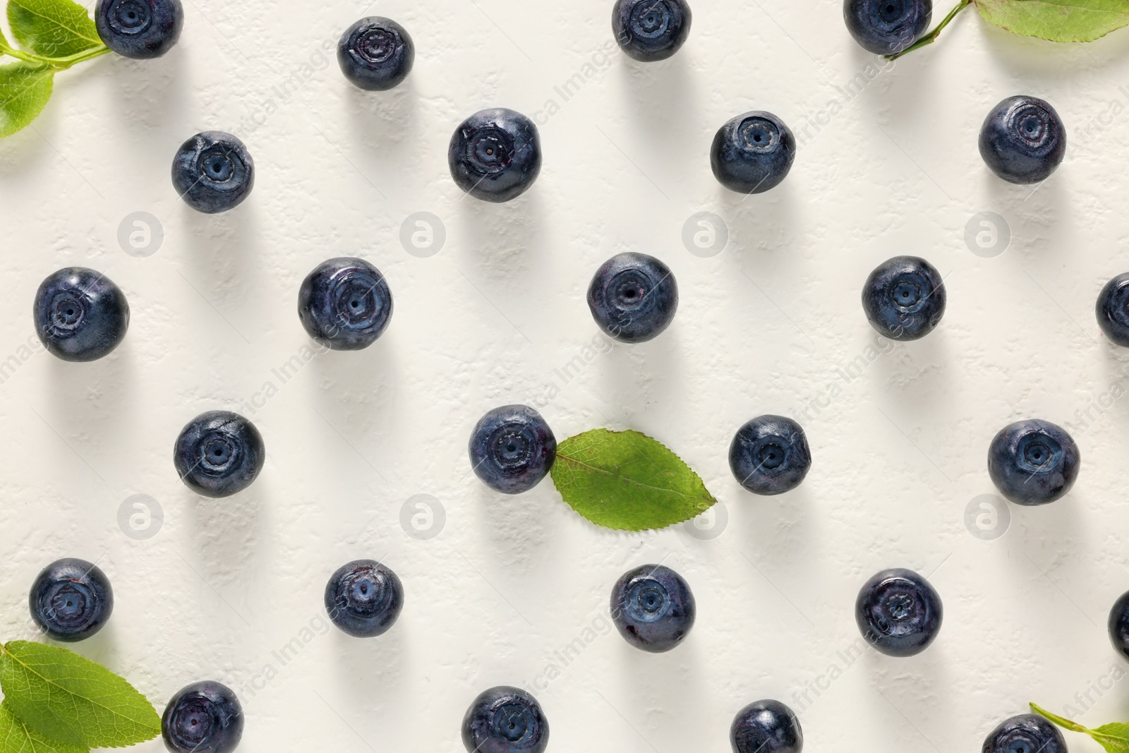 Photo of Tasty fresh bilberries with green leaves on white table, flat lay