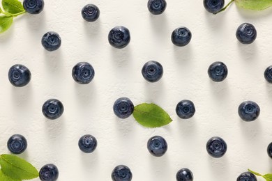 Tasty fresh bilberries with green leaves on white table, flat lay