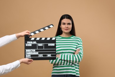 Photo of Actress performing while second assistant camera holding clapperboard on beige background. Film industry