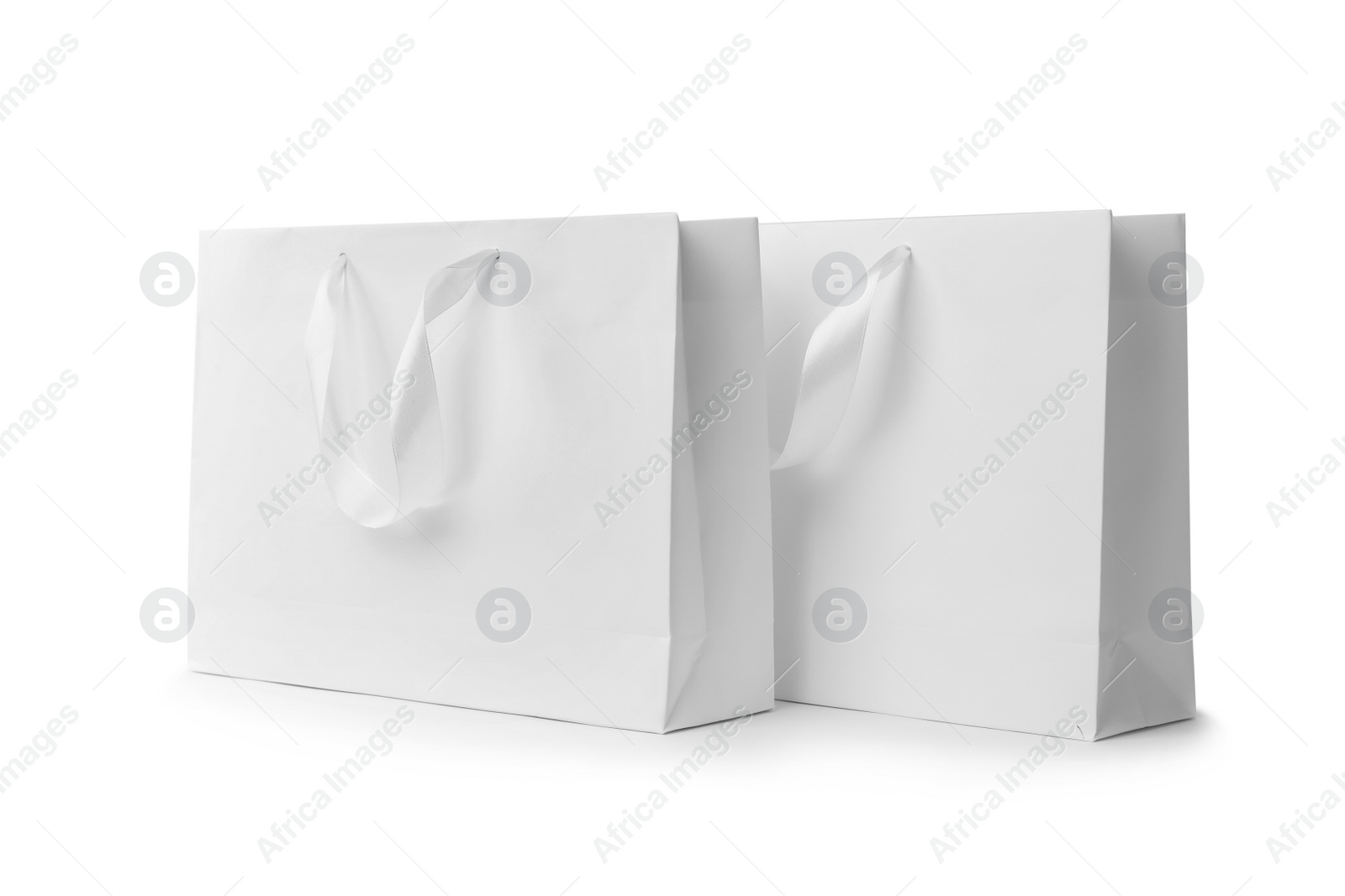 Photo of Paper shopping bags with ribbon handles on white background. Mockup for design