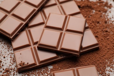 Photo of Delicious milk chocolate and cocoa powder on table, closeup