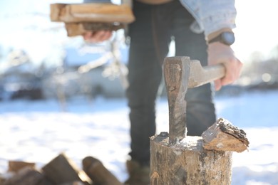 Photo of Man taking axe out of wooden log outdoors on winter day, closeup. Space for text