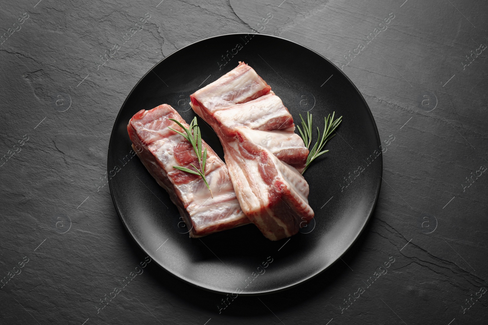 Photo of Raw ribs with rosemary on black table, top view