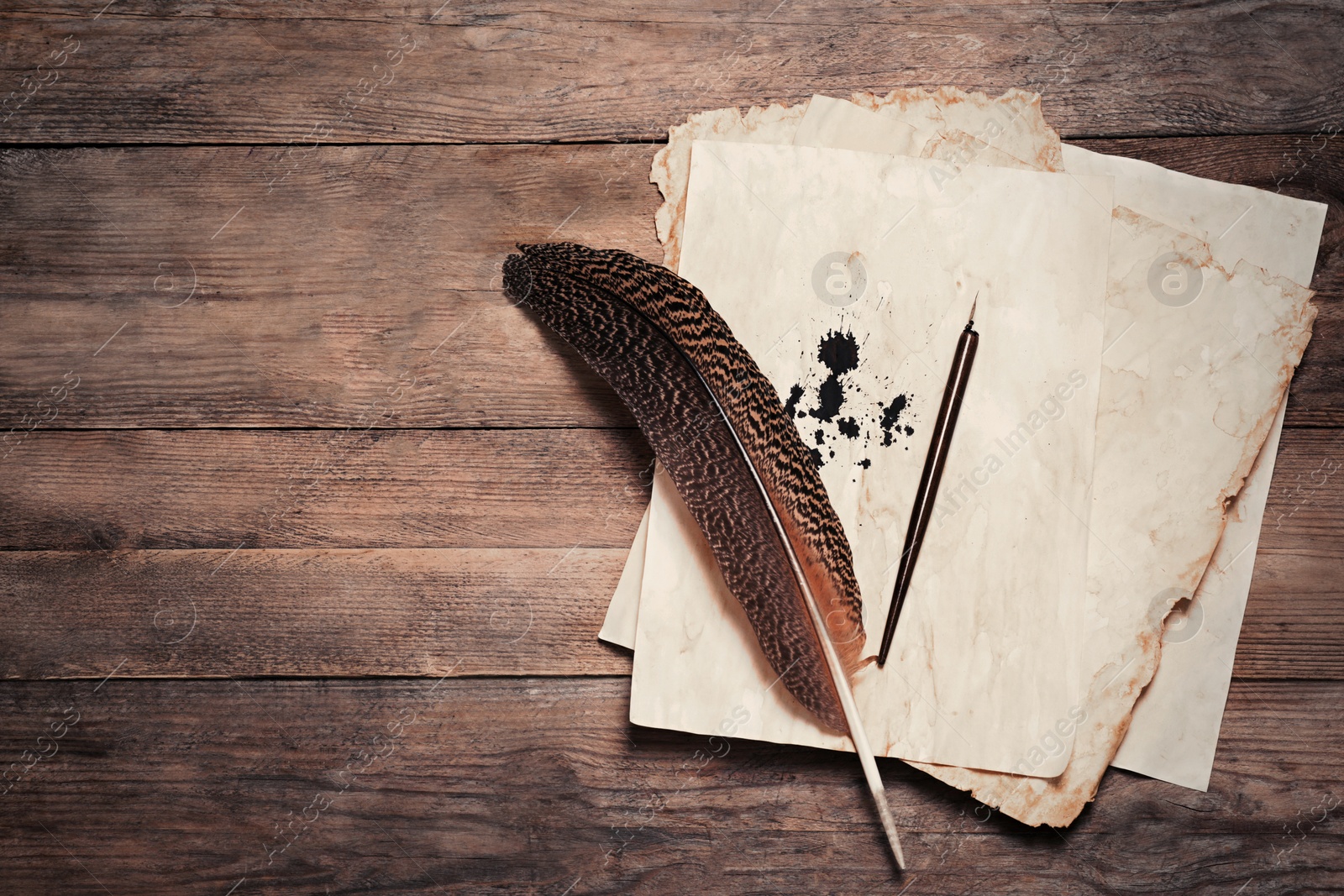 Photo of Feather, fountain pen and vintage parchment with ink stains on wooden table, top view. Space for text