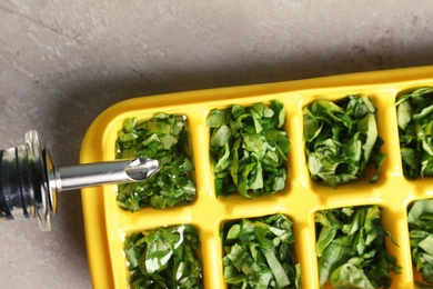 Photo of Pouring oil into ice cube tray with spinach on grey background, top view