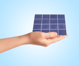 Woman demonstrating solar panel on light blue background, closeup. Alternative energy source 