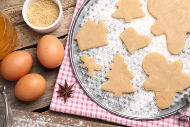 Photo of Ingredients and raw Christmas cookies in different shapes on wooden table, flat lay