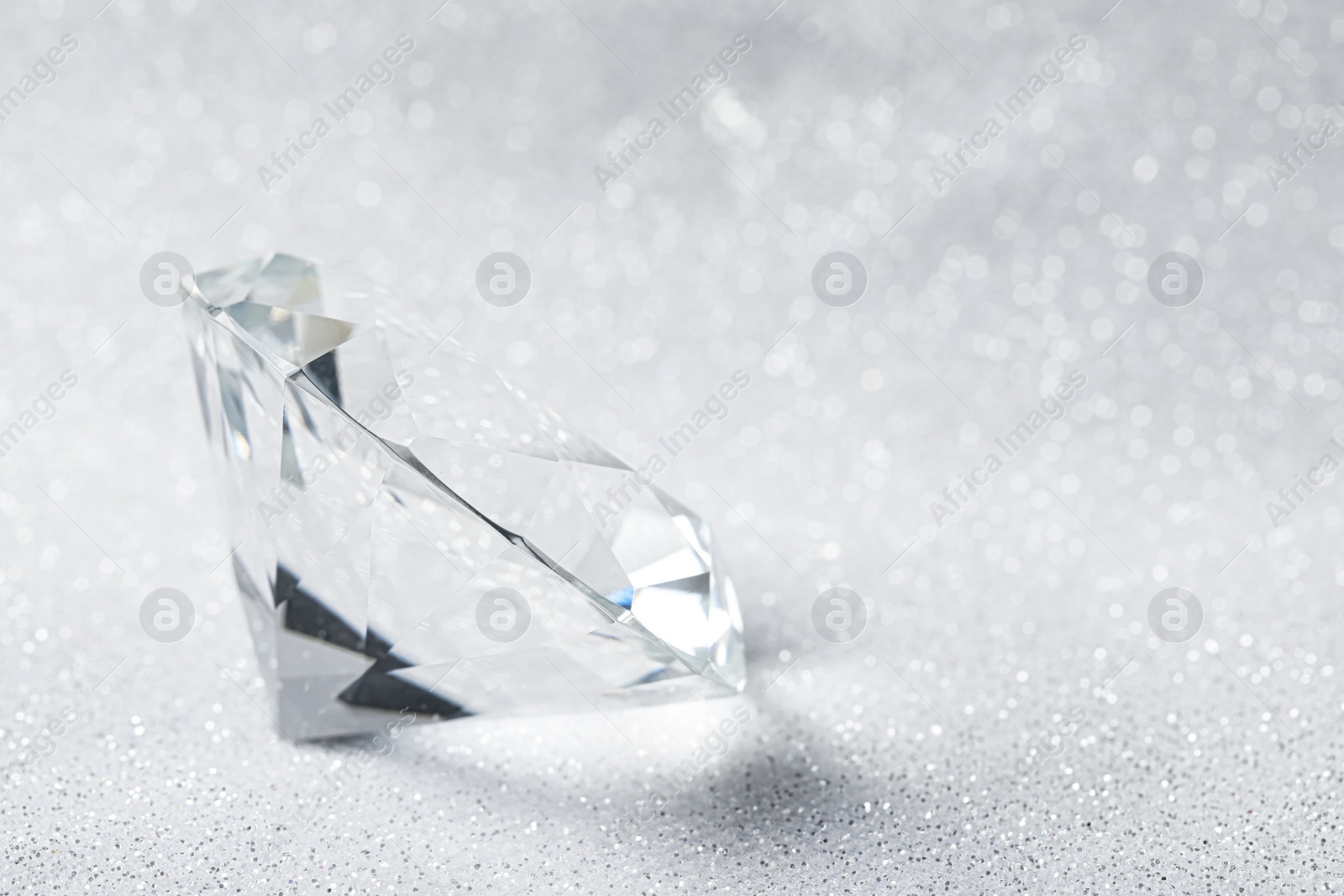 Photo of Beautiful dazzling diamond on shiny glitter background, closeup. Space for text