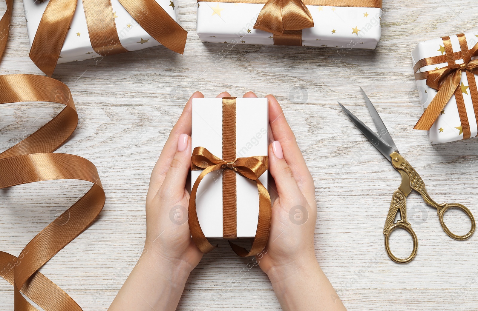 Photo of Christmas present. Woman with gift boxes, ribbon and scissors on white wooden background, top view