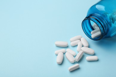 Photo of Vitamin pills and bottle on light blue background, closeup. Space for text