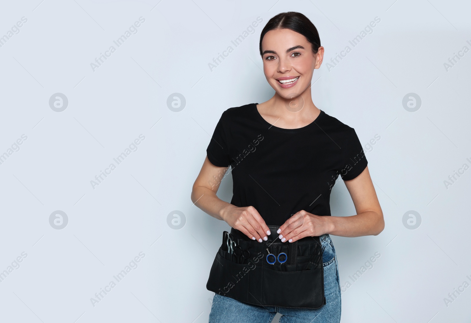 Photo of Portrait of happy hairdresser with professional tools on light background, space for text